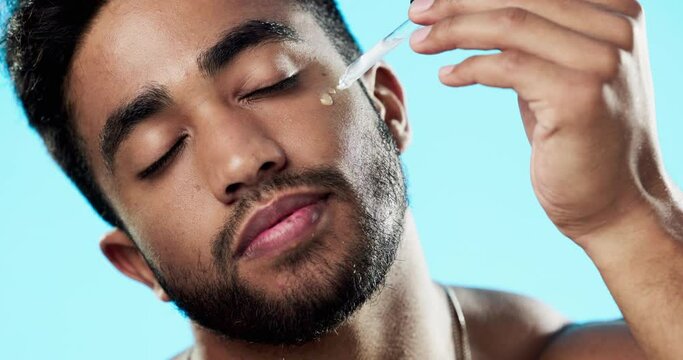 Skincare, health and man with face serum in a studio with a beauty, grooming and face routine. Wellness, cosmetic and male model with a facial oil pipette for a skin treatment by a blue background.