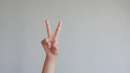 Young girl raising two fingers up on hand it is shows peace strength fight or victory symbol and letter V in sign language on gray background.