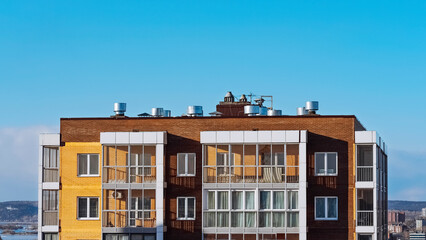 A modern house with a flat roof, air ducts and air conditioners above a modern apartment building....