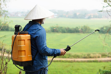Asian farmer uses herbicides, insecticides chemical spray to get rid of weeds and insects or plant...