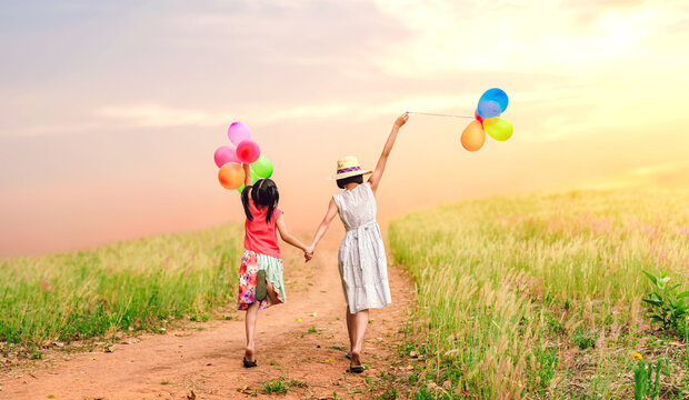 Happy Two children girls holding balloons walking on meadow trail springfield sunset background.