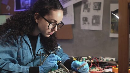 Electrician with soldering iron repairs computer circuit board in retro workshop. Technician engineer in workshop takes tin with a soldering iron and puts it on microcircuit.