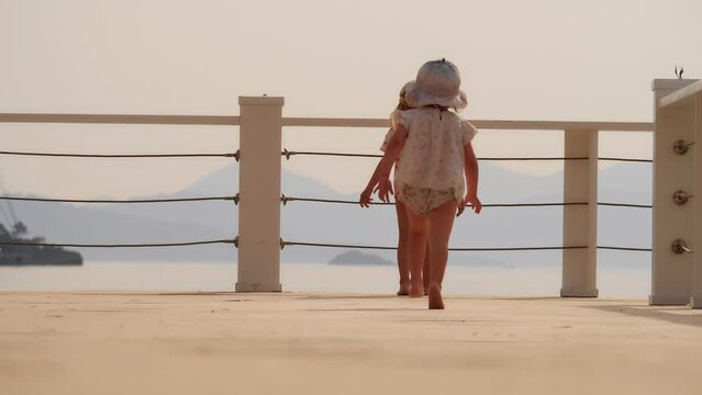 Two little girls run towards sea along jetty, slow motion. Discovery concept