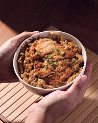 Hands grabbing a bowl of japanese katsudon