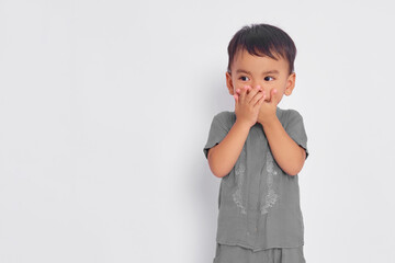 Shocked toddler Asian muslim boy covering mouth with hands and looking at empty space isolated on...