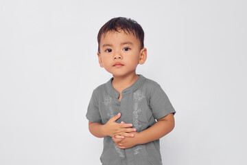 Toddler Asian muslim boy keeping both hands on belly, feeling hungry and wanting to eat delicious...