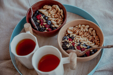 Bowl breakfast with porridge, fruits, berries and nuts and tea is on a tray