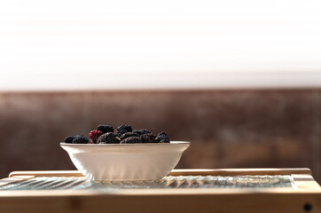 A bowl of fresh mulberries on the table near the window.