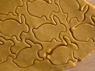 Close-up kneaded ginger dough and carved figurines from it. The shapes of rabbit. Cutting sugar cookie dough with Easter shaped cookie cutters. Preparation for Easter. Holidays baking.