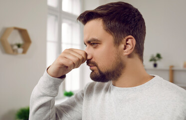 Man smells something bad at home. Young man pinches his nose as he feels a bad, unpleasant smell of...