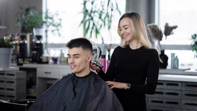 A handsome young man in a barbershop. A woman hairdresser cuts a client, smiles, communicates