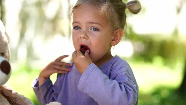 Little girl eating strawberries in the garden near the teddy bear