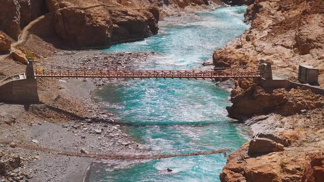 4K shot of old and new foot bridges above the blue Tsarap river flowing in between mountains on the way towards the Phugtal Monastery near Purne village in Zanskar, Himachal Pradesh, India.