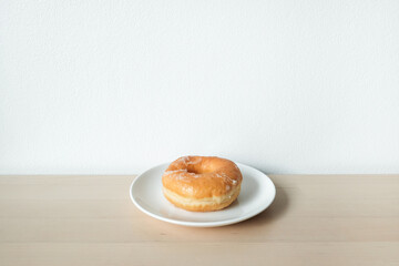 Sweet delicious glazed donut on white plate.
