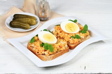 Egg salad over brown bread and cut egg on white table.  Homemade spread made from eggs, vegetable and mayonnaise. Decorated healthy young buckwheat.