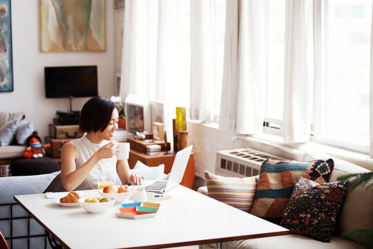 Happy Woman Holding Coffee Cup While Using Laptop At Home