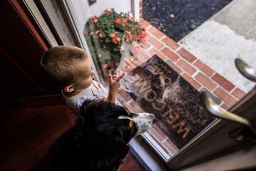 Toddler boy and dog look out front door together
