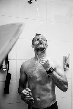 A man surfer washes in an outdoor shower after surfing.
