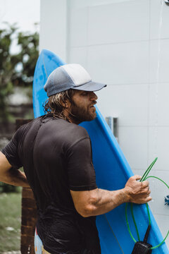 A man surfer washes in an outdoor shower after surfing.