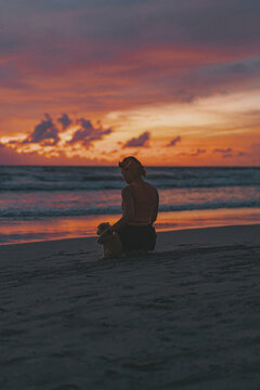 Woman with a puppy on the beach watching the sunset.
