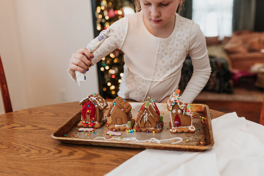 Young girl decorates gingerbread houses at kitchen table