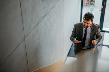 Handsome businessman typing on his smartphone and walking up the stairs in a bright venue. Copy...