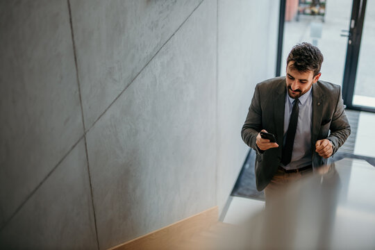 Handsome businessman typing on his smartphone and walking up the stairs in a bright venue. Copy space 