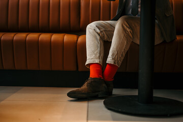 A man sitting in the cafe, wearing pants, orange socks, and shoes. Focus on legs only