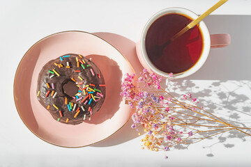 Chocolate donut with sprinkles on a plate and a cup of tea, delicious breakfast