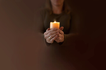 Kobieta modli się trzymając w dłoniach zapaloną świecę. Zmartwychwstanie pańskie wiara i nadzieja w modlitwie - obrazy, fototapety, plakaty