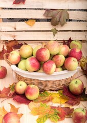  On a wooden texture table there is a wicker small basket in which ripe red apples lie.