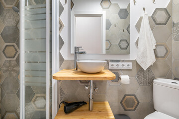 Gray polygonal ornamental tiles in bathroom with a glassed-in shower and vanity sink. Concept of stylish designer bathroom in an apartment or country house