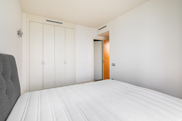Modern bright bedroom with a bed and built-in wardrobe and an open door to the corridor. Minimalistic but cozy design concept. Hotel or rental apartment design