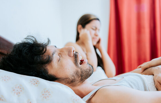 Snoring man in bedroom and wife covering her ears. Husband snoring while the wife suffers and covers her ears. Sleep apnea concept