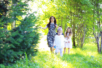 Young large family on a summer morning walk. Beautiful mother with children is playing in the park.