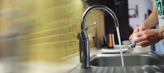 People are washing the dishes . Cleaning solution.A white bottle with dishwashing gel, sponges and rubber gloves on the background of a sink with dirty dishes.