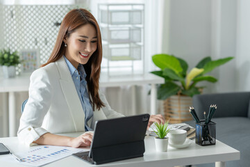 Beautiful Asian businesswoman sitting at work saving data Happy checking financial details on laptop computer in the office.