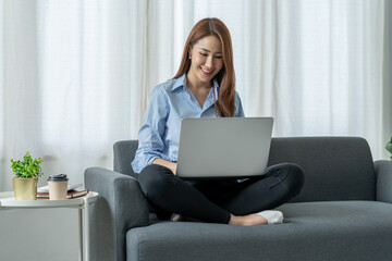 Naklejka premium modern work lifestyle Asian businesswoman sitting on the sofa at home working on a laptop online using free space internet to get information in order to shop online happily.
