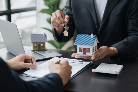 Real Estate Agents, Insurance Sales Agents, And Young Asian Businessmen Handing Home Keys And Model Homes To Homebuyers After Signing Sales Contracts Are Satisfied In The Office.