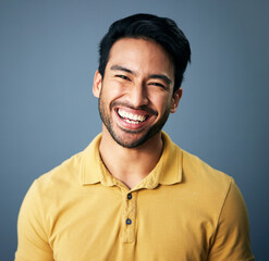 Portrait, happy and carefree with a man in studio on a blue background feeling confident or positive. Face, smile and cheerful with a handsome young male posing on a color wall looking relaxed