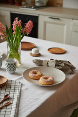 Festive table setting with pink flowers and donuts on a plate in the kitchen