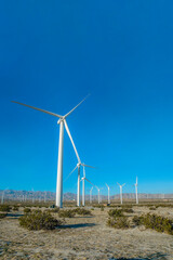 Windmills on vast dry land with mountain and blue sky view in the background. The windpumps have three blades that produce renewable energy using wind power.