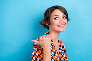 Portrait of cute cheerful girl beaming smile look direct finger empty space isolated on blue color background