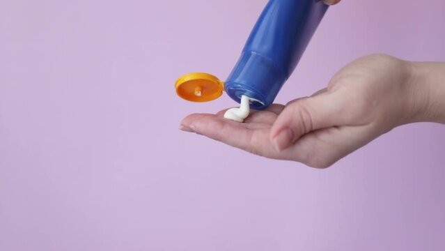 a woman's hand squeezes sun protection cream from a bottle