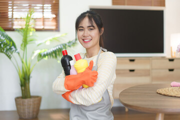 Maid holding cleansing bottles and showing thumb up after cleaning and wiping the dirty in home