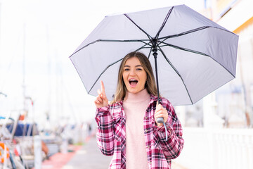 Young pretty Romanian woman holding an umbrella at outdoors pointing up a great idea