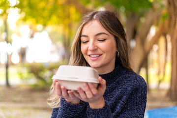 Young pretty Romanian woman holding a burger at outdoors