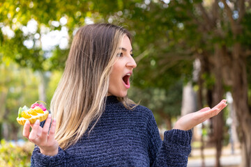 Young pretty Romanian woman holding a tartlet at outdoors with surprise facial expression