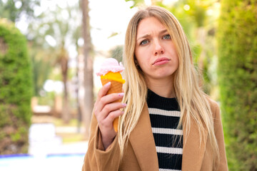 Young pretty blonde woman with a cornet ice cream at outdoors with sad expression