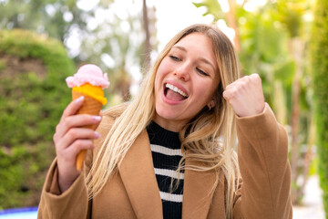 Young pretty blonde woman with a cornet ice cream at outdoors celebrating a victory